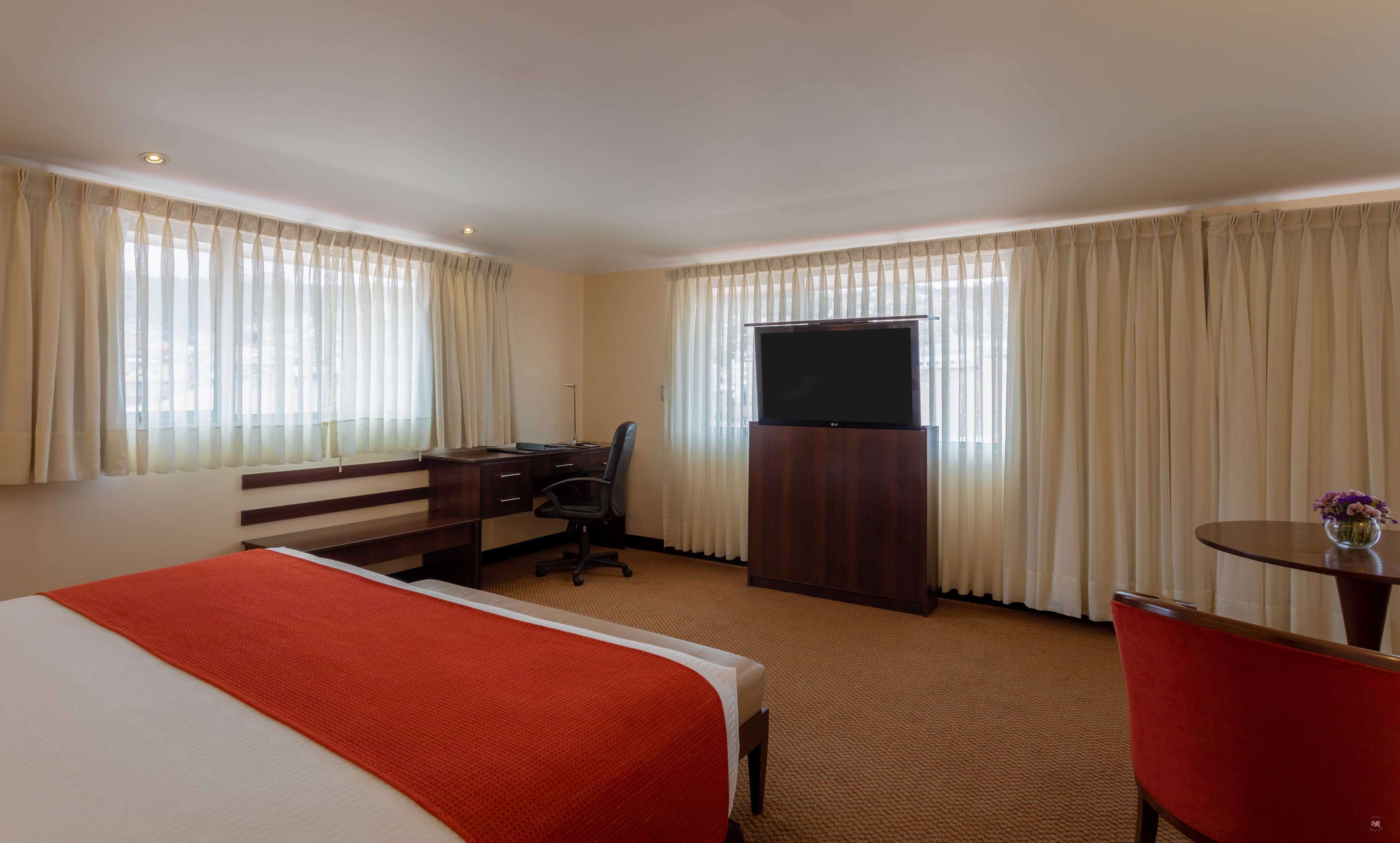 A hotel room with a bed, desk, chair, TV, and curtains.