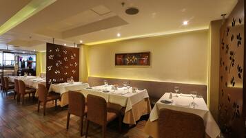A restaurant with multiple tables set for dining, wooden flooring, and a decorative wall with leaf patterns.