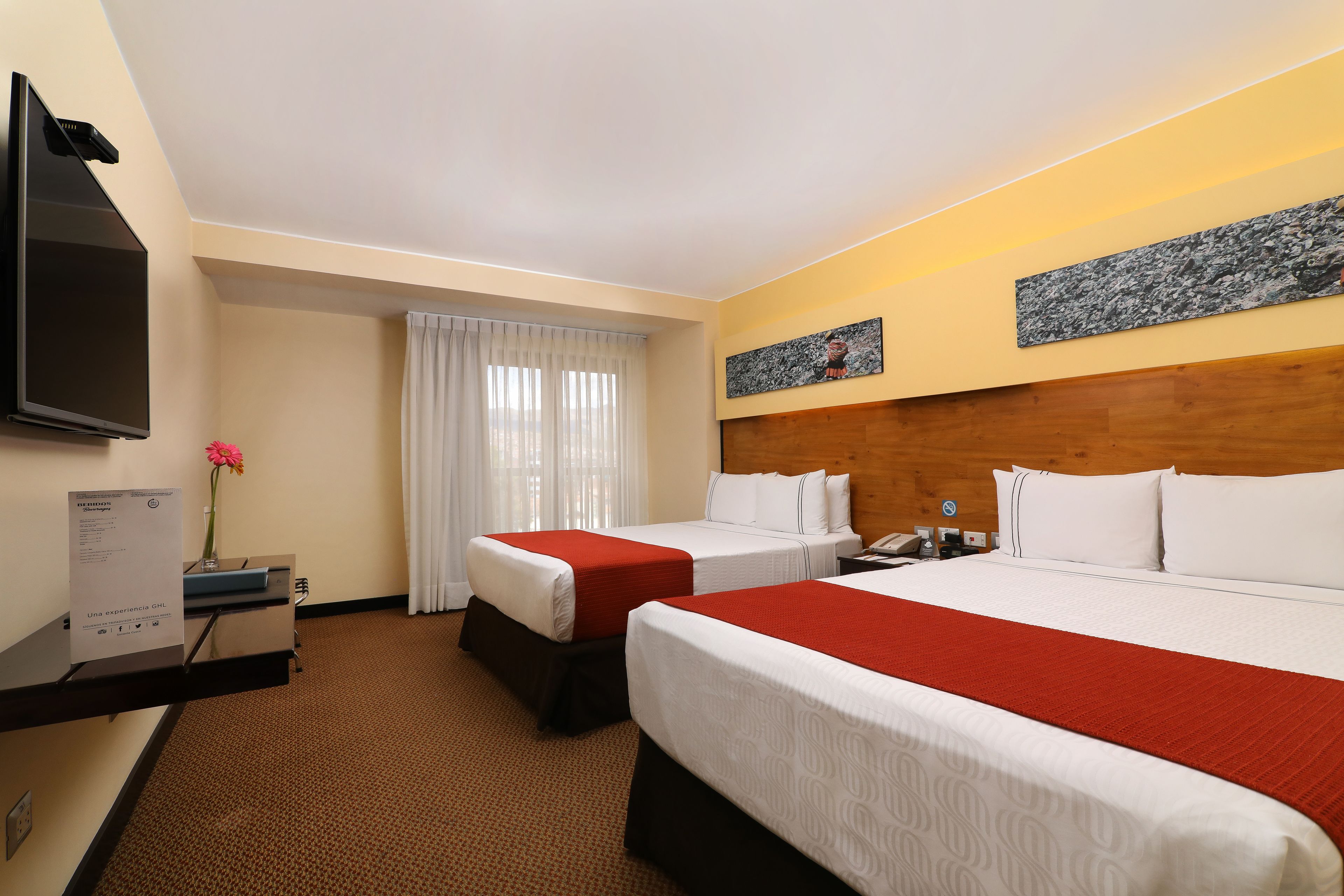 Een hotelkamer met twee bedden, een flatscreen televisie, een bureau met computer en een raam met gordijnen.