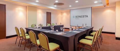 Une salle de conférence équipée d’une longue table, de chaises et d’un écran de projection affichant le texte « SONESTA CUSCO ».