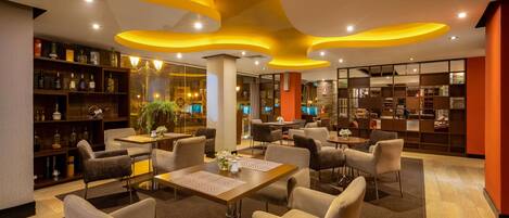 Un hall de hotel moderno con mesas redondas, asientos cómodos y una paleta de colores cálidos.