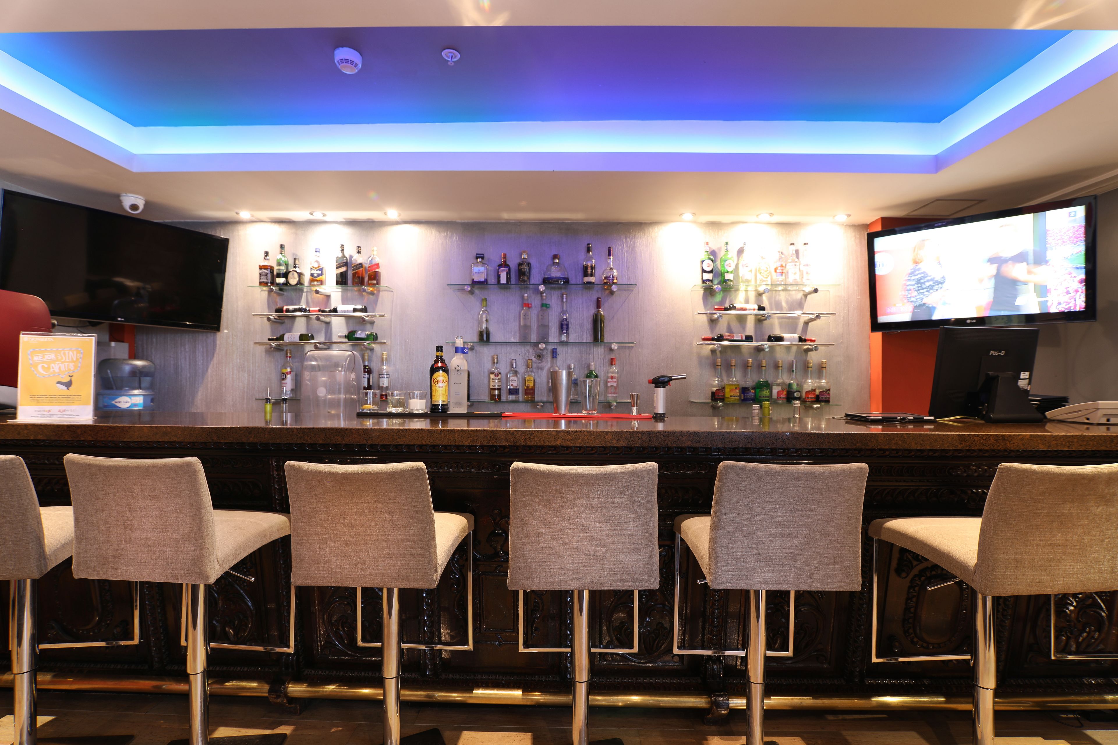 A bar area with a counter, multiple shelves of bottles, a television, and bar stools.