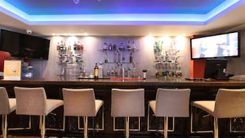Zona de bar con mostrador, varias estanterías llenas de botellas, un televisor y taburetes.
