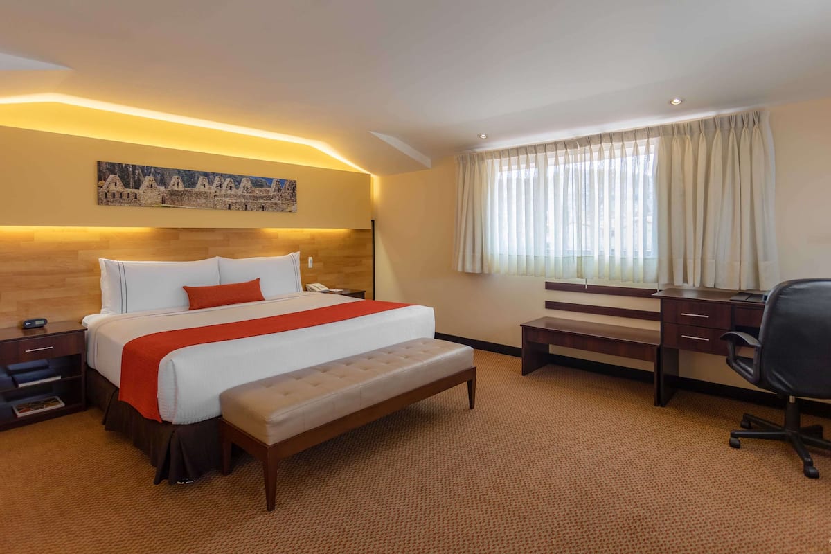 Une chambre d’hôtel avec un grand lit, un bureau, une chaise et une fenêtre avec des rideaux.