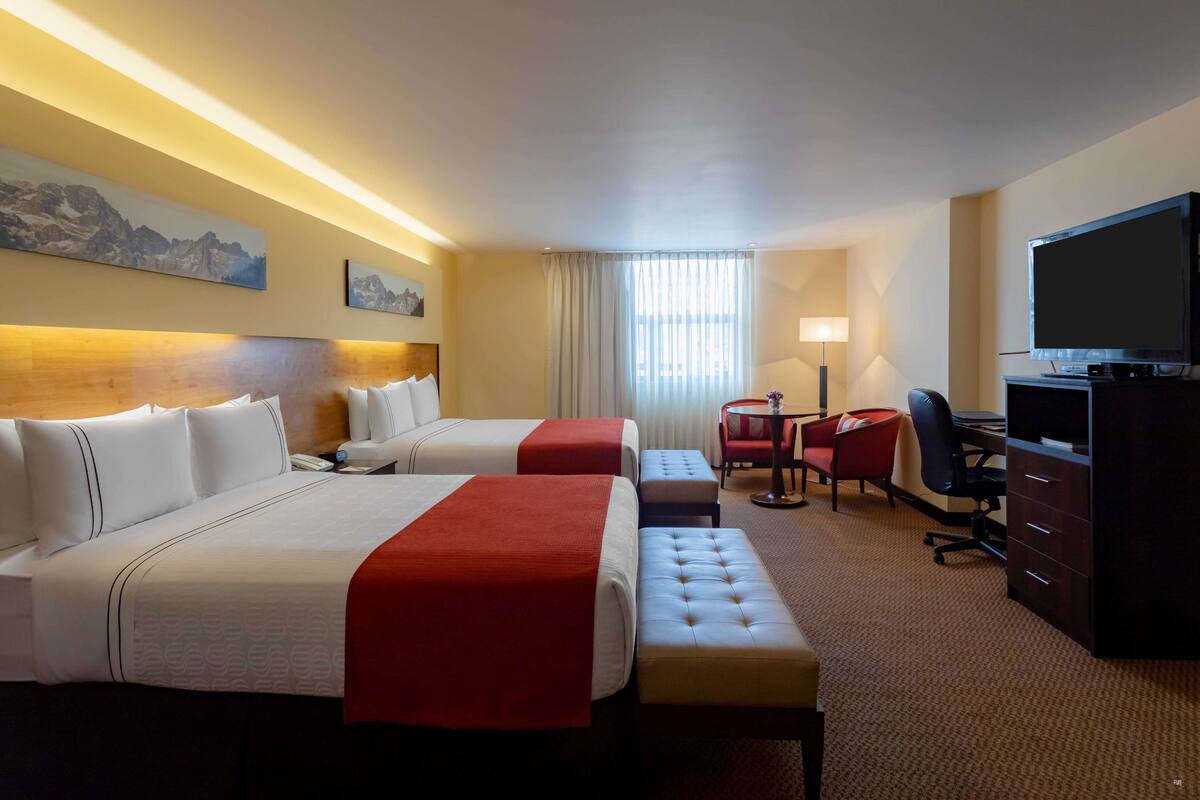 Ein Hotelzimmer mit zwei Betten, einem Schreibtisch, einem Stuhl, einem Fernseher und einer Lampe.