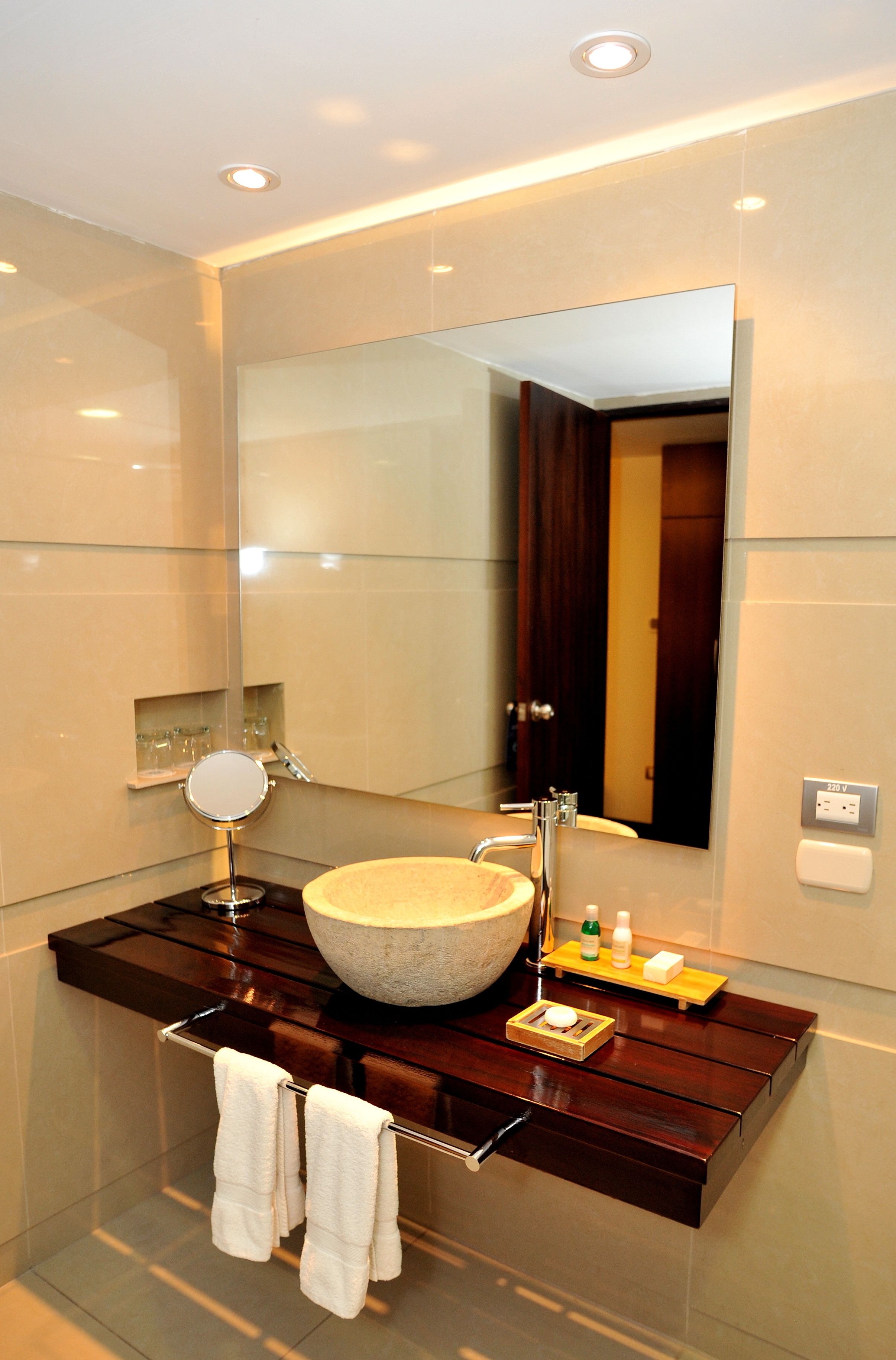 Un baño moderno con un espejo grande, un lavabo redondo y un mueble de tocador de madera.