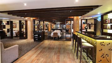 Un amplio vestíbulo de hotel con piso de madera, una zona de bar con taburetes y una sección de comedor con mesas y sillas.
