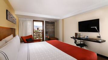 A hotel room with a large bed, a desk with a computer, a TV, and a view of the outdoors.