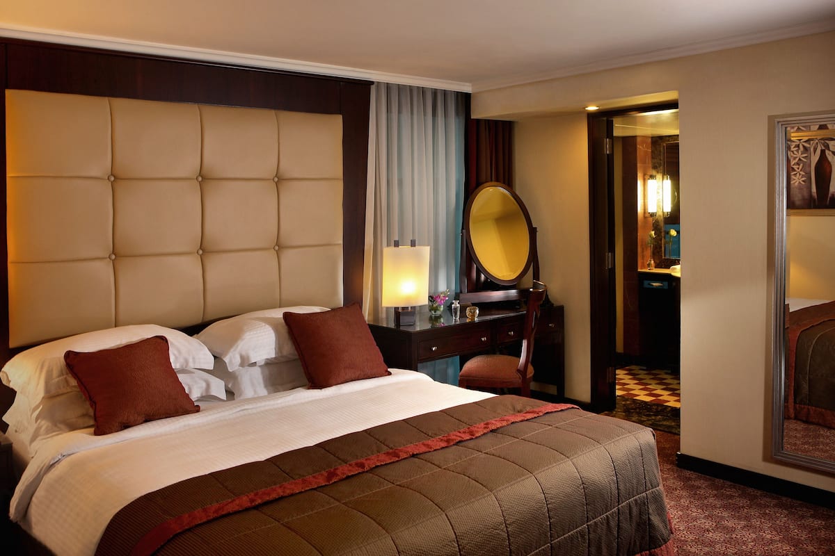 Habitación de hotel con una cama grande, una mesita de noche con lámpara, un espejo y una silla.