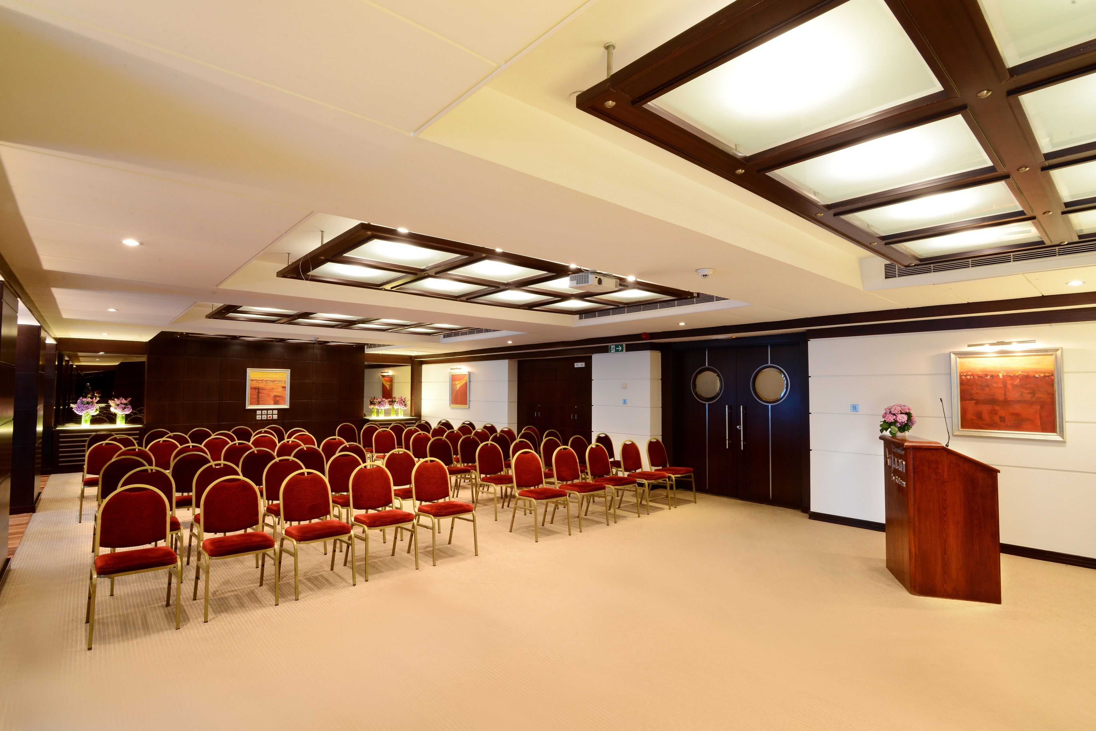 A conference room with rows of red chairs, a podium, and a ceiling with skylights.