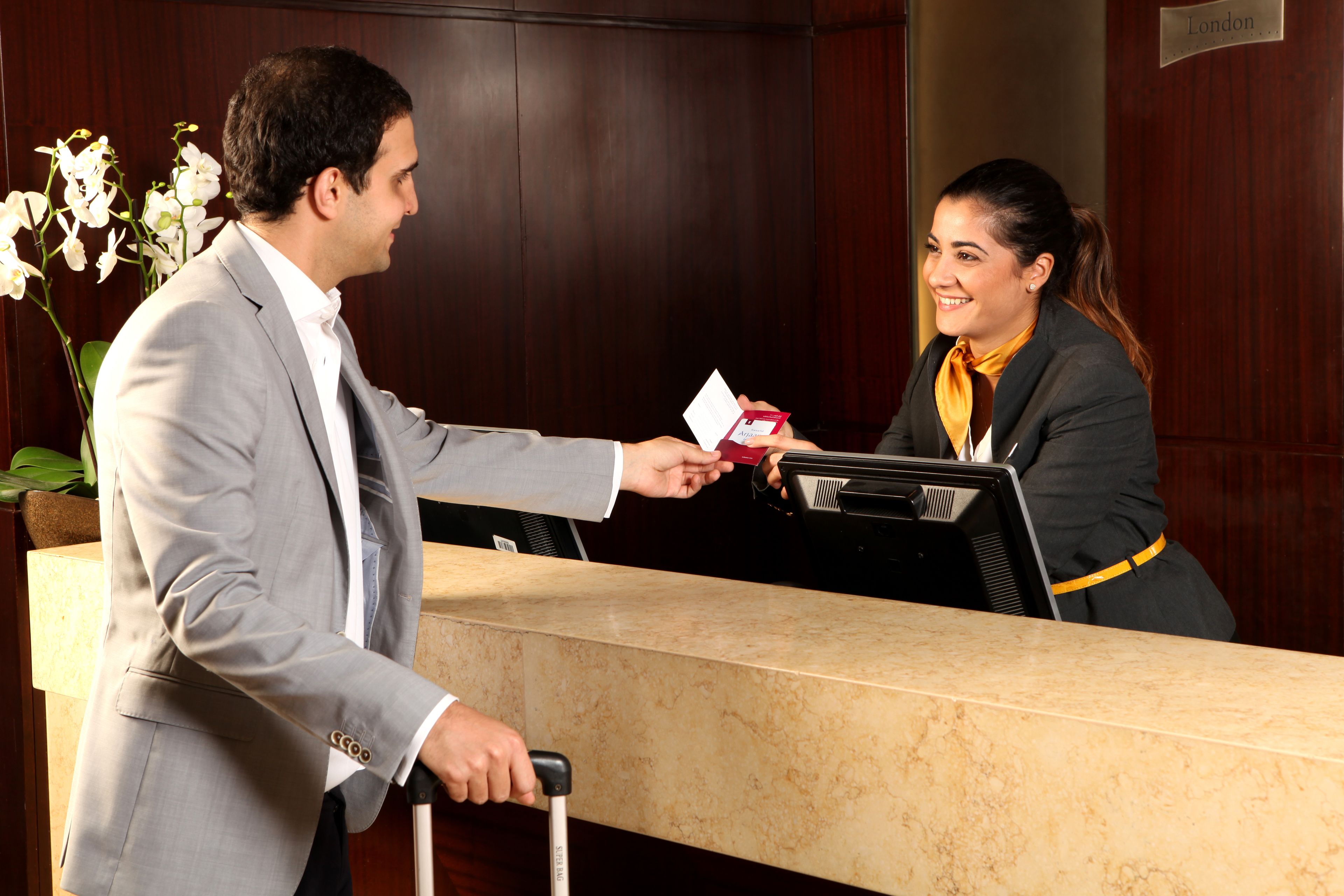 A hotel reception desk with a marble counter, a potted orchid, and a sign indicating the location as London.