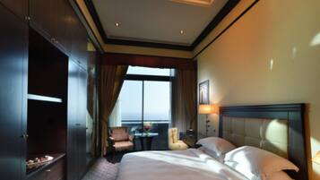 Habitación de hotel con una cama grande, un armario, un área de estar con una mesa y sillas, y vistas al exterior a través de una ventana.