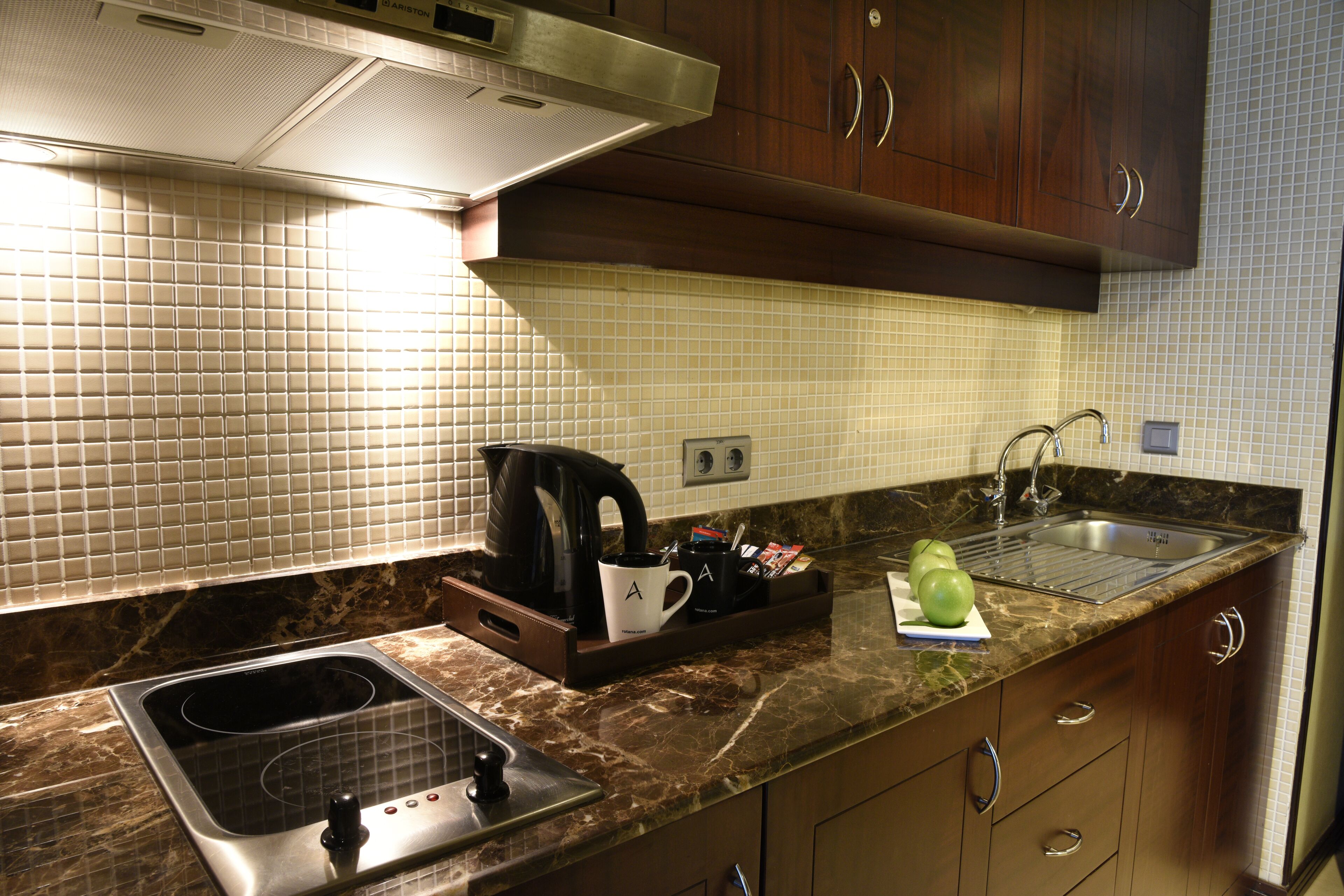 Una cocina con lavamanos, estufa y cafetera sobre la encimera.