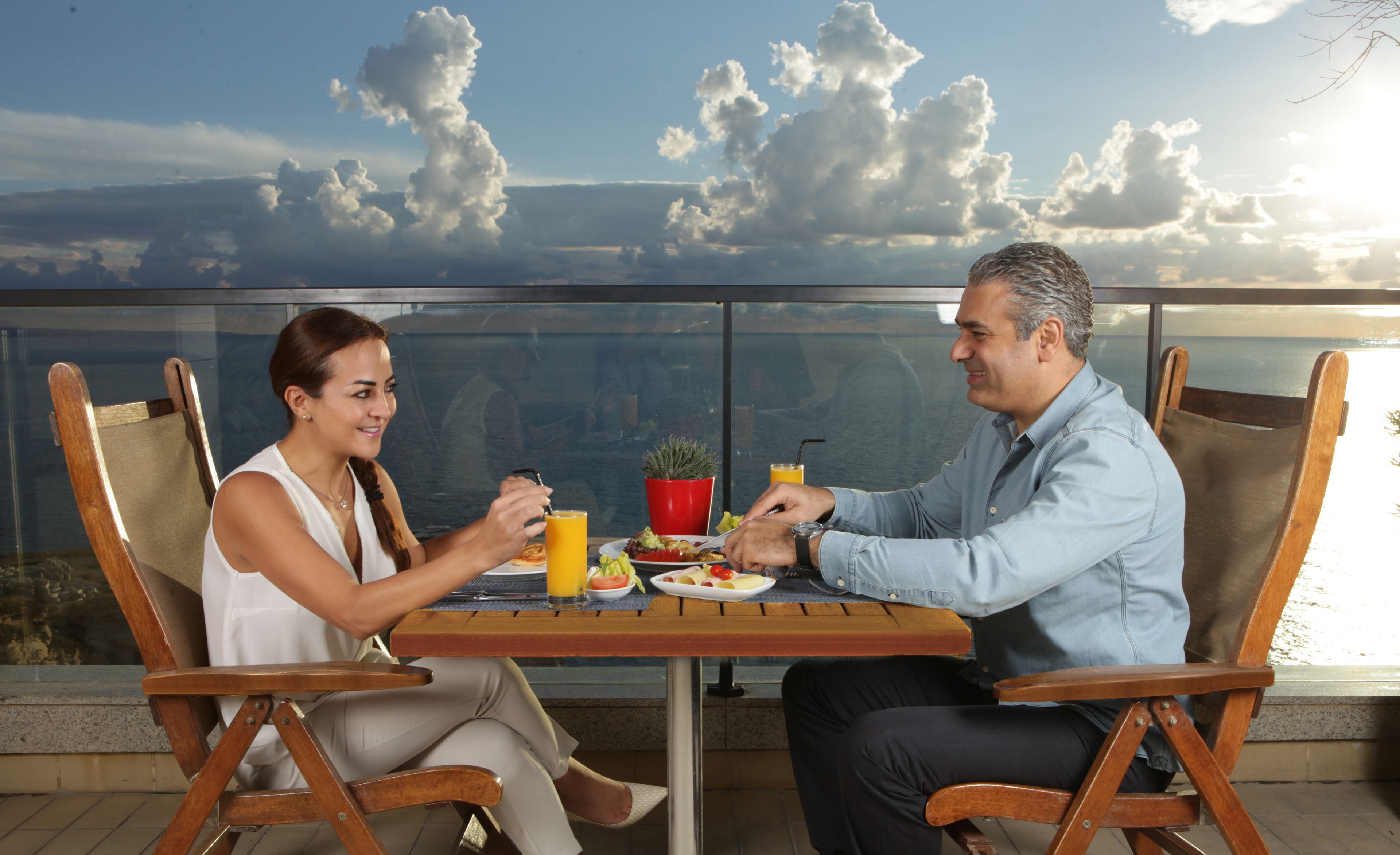 Deux personnes dînent à une table en plein air, profitant d’une vue magnifique sur le ciel et les nuages.