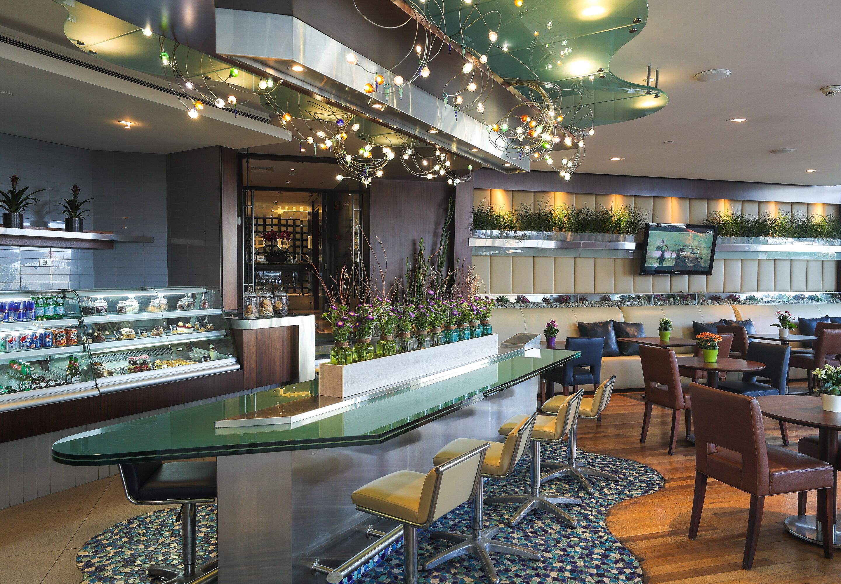 A modern hotel lobby with a glass bar, seating area, and a television mounted on the wall.