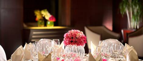 Mesa redonda para comer dispuesta con servilletas blancas, varias copas de vino y un centro de mesa con rosas rosadas.