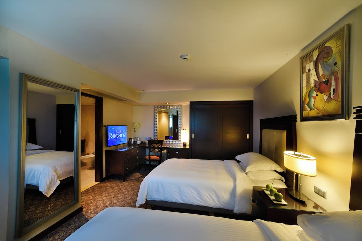 Habitación de hotel con dos camas, un escritorio con computadora, un espejo y un cuadro en la pared.