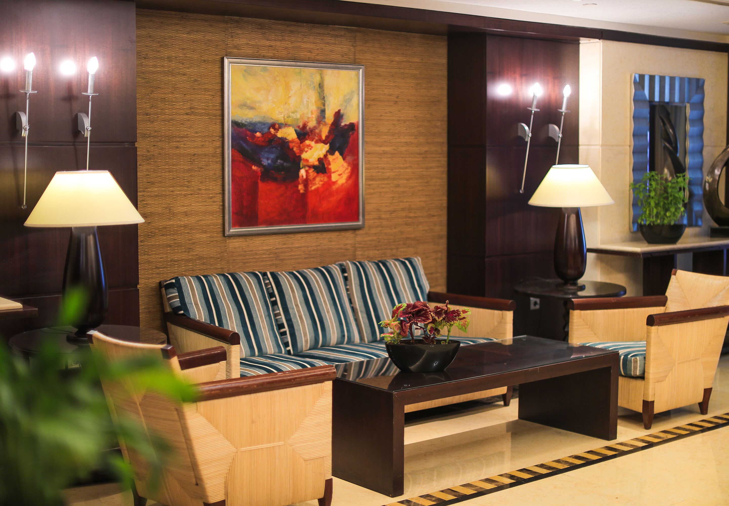 A lobby with a striped sofa, two armchairs, a coffee table with a flower vase, and wall-mounted lamps.