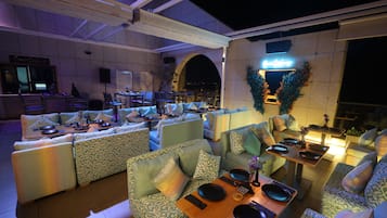 An outdoor dining area with multiple seating arrangements and tables set for dining, featuring a modern design with patterned cushions and ambient lighting.
