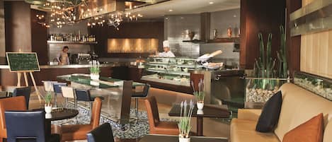 A modern restaurant interior with a bar area, seating arrangement, and a chef preparing food.