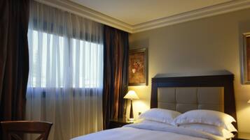 A hotel room with a large bed, a chair, a nightstand with a lamp, and a painting on the wall.