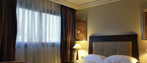 A hotel room with a large bed, a chair, a nightstand with a lamp, and a painting on the wall.