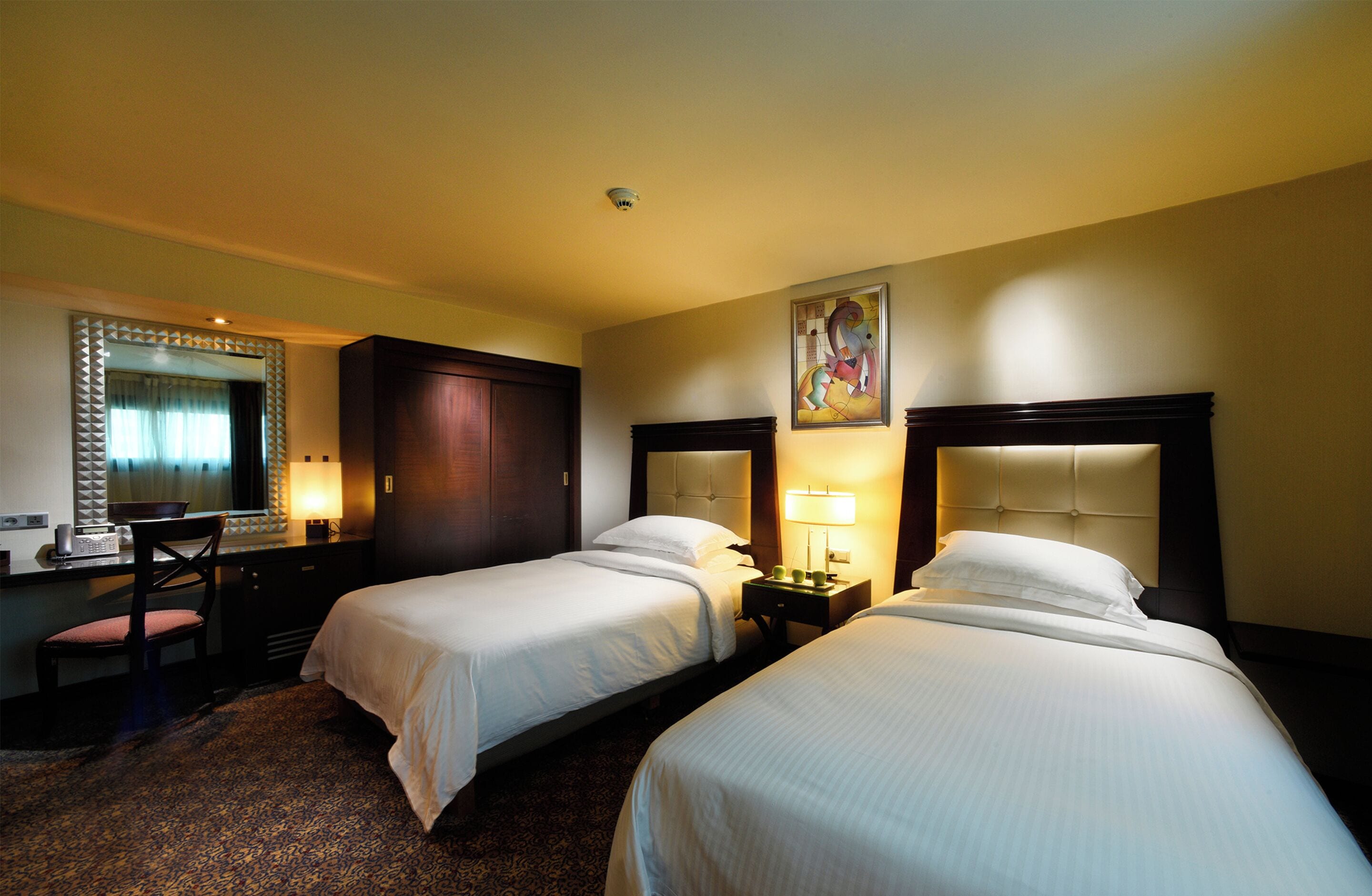 A hotel room with two beds, a desk with a chair, a mirror, and a painting on the wall.