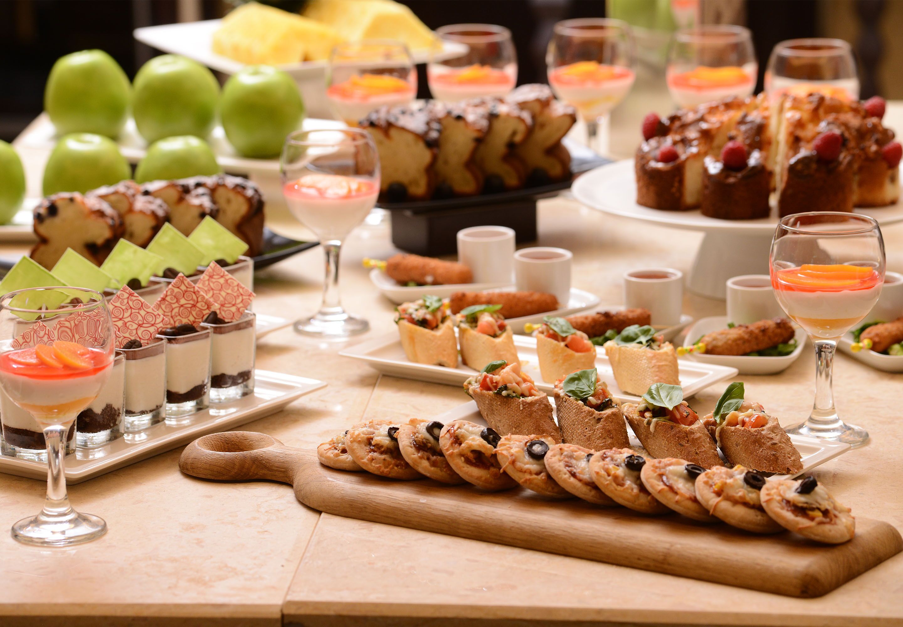 A variety of desserts and appetizers on a buffet table, including cakes, pastries, and fruit.
