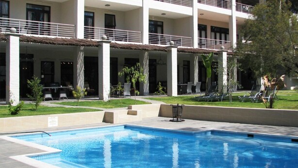 A swimming pool area with lounge chairs and a building with balconies in the background. - Sandton Lodge Rivonia (Sandton)