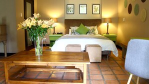 A hotel room with a bed, bedside tables, a wooden table, a chair, and a vase of flowers. - Sandton Lodge Rivonia (Sandton)