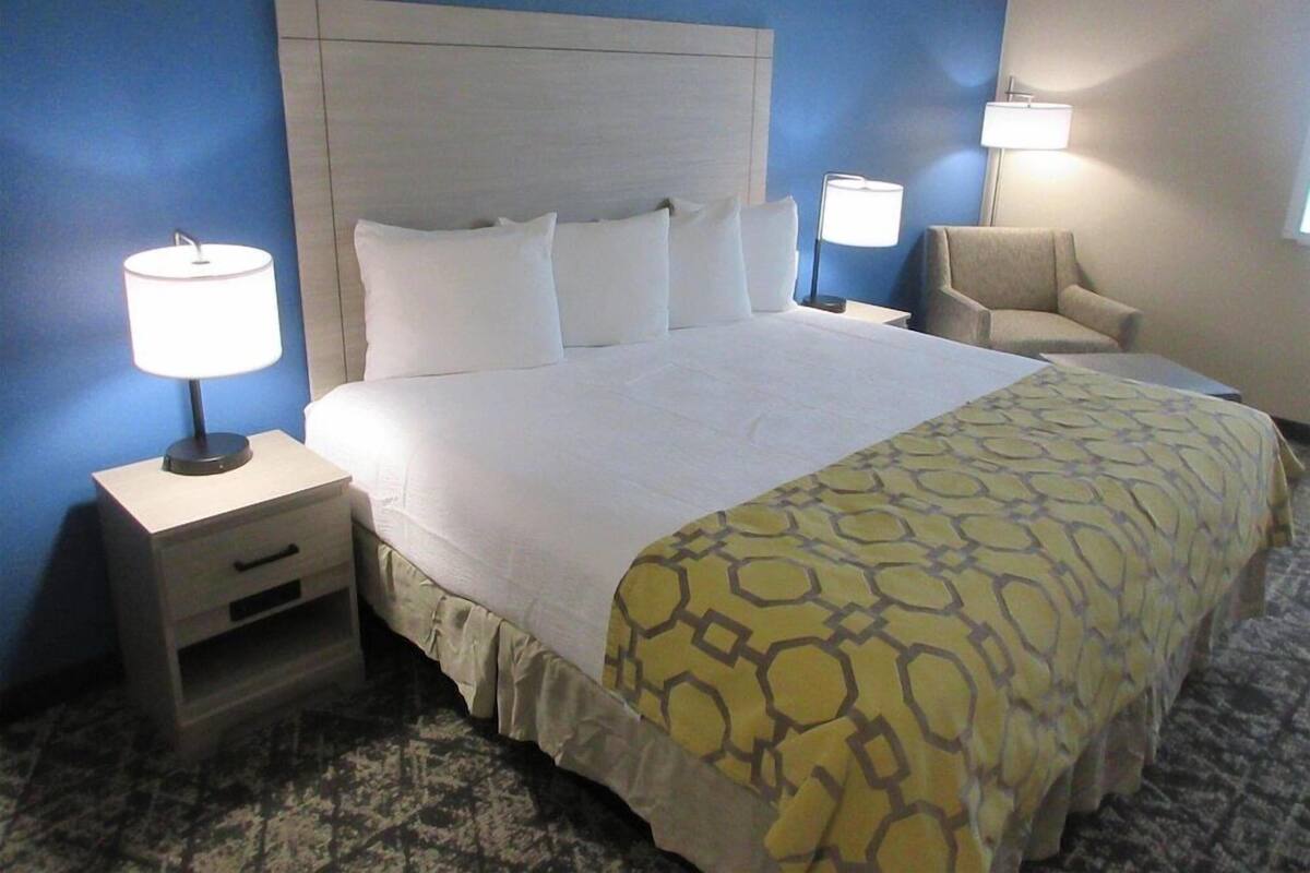A hotel room with a large bed, two bedside tables with lamps, a chair, and a patterned bedspread.