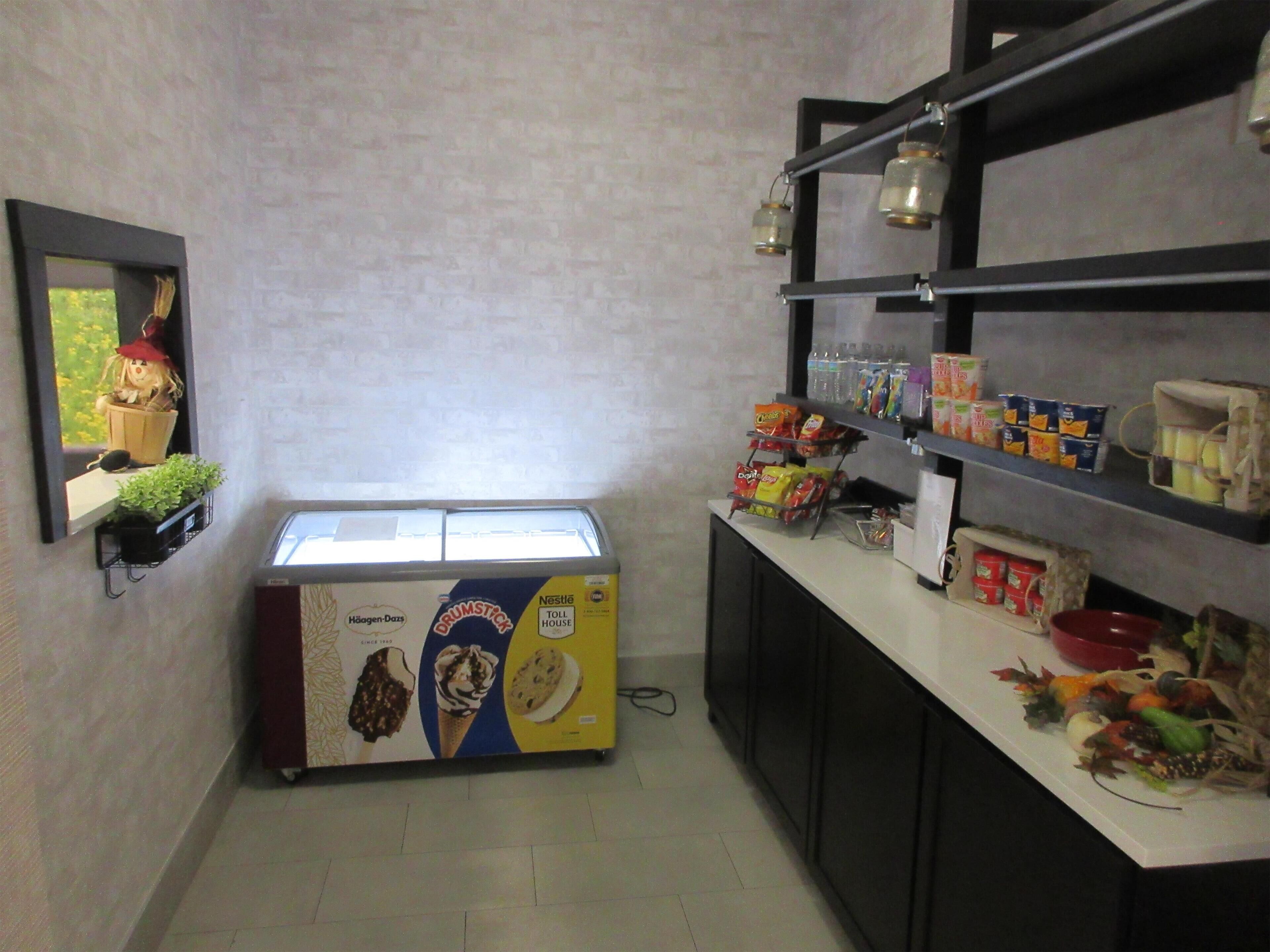 A small kitchenette with a refrigerator, a shelf with snacks, and a window with a view of greenery.