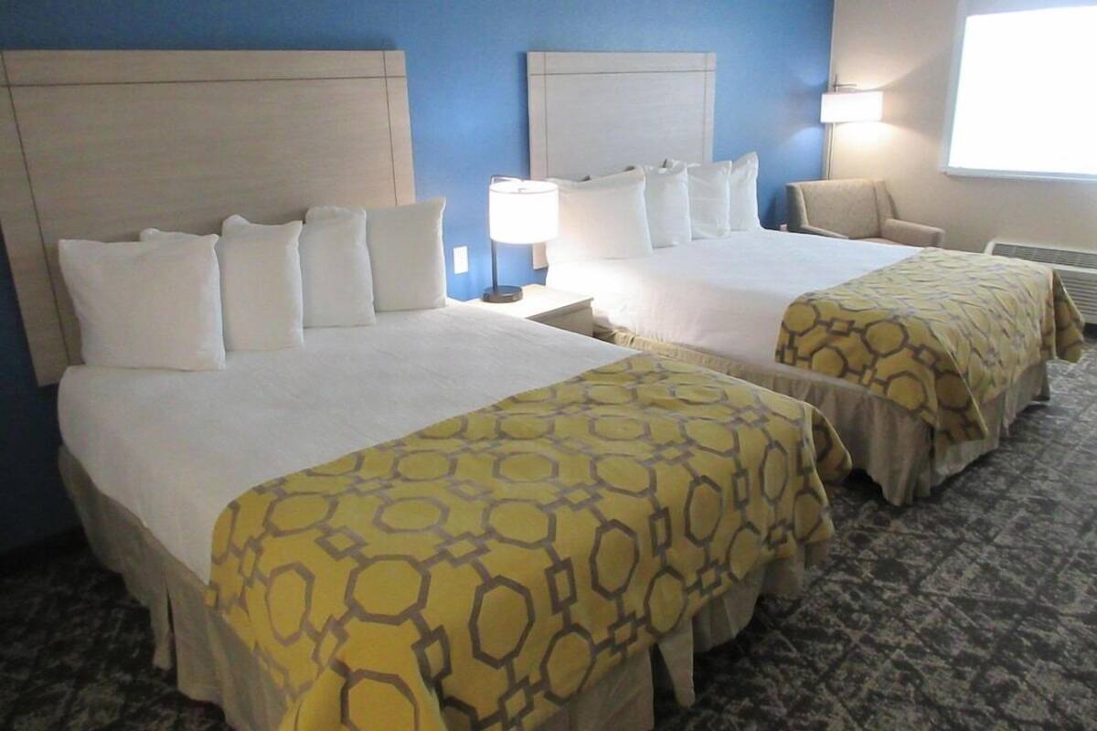 A hotel room with two beds, a nightstand, a lamp, and a window.
