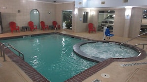 An indoor swimming pool with a hot tub, surrounded by red and blue chairs, and a tiled wall with a window. - Best Western Decatur Inn (Decatur)