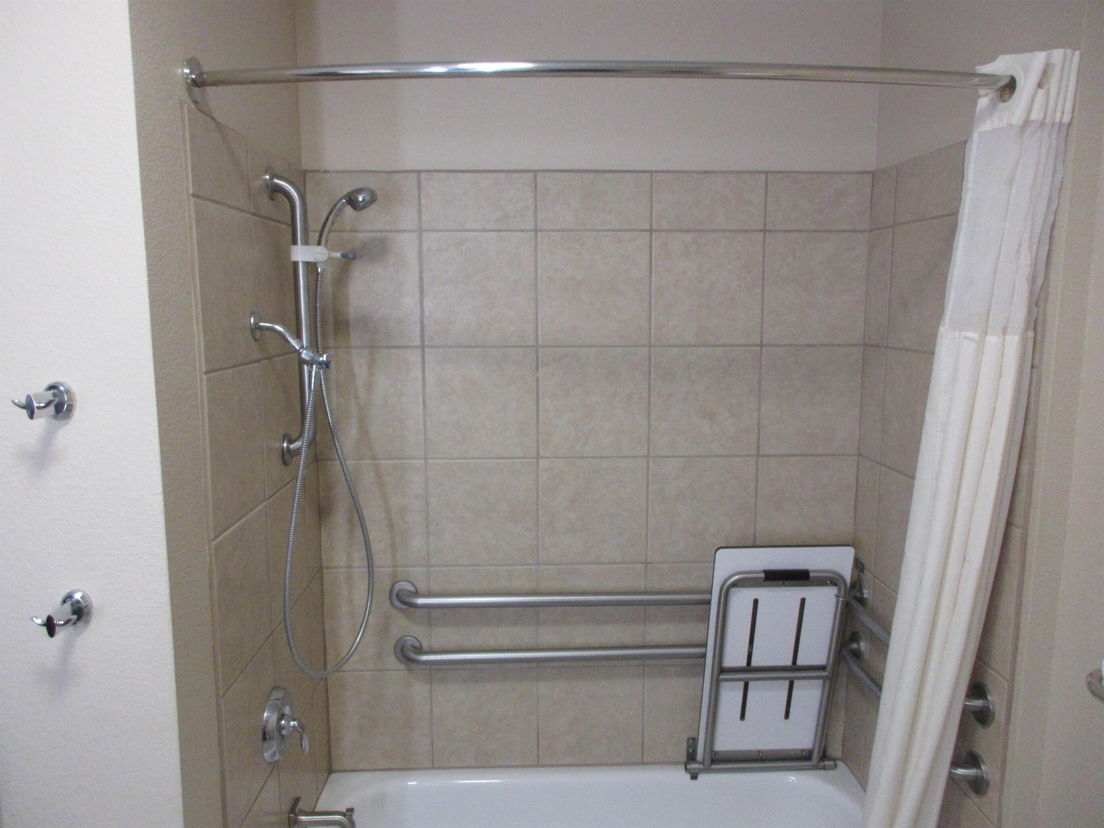 A shower area with a glass door, a handheld showerhead, a handheld shower nozzle, a grab bar, and a towel rack.