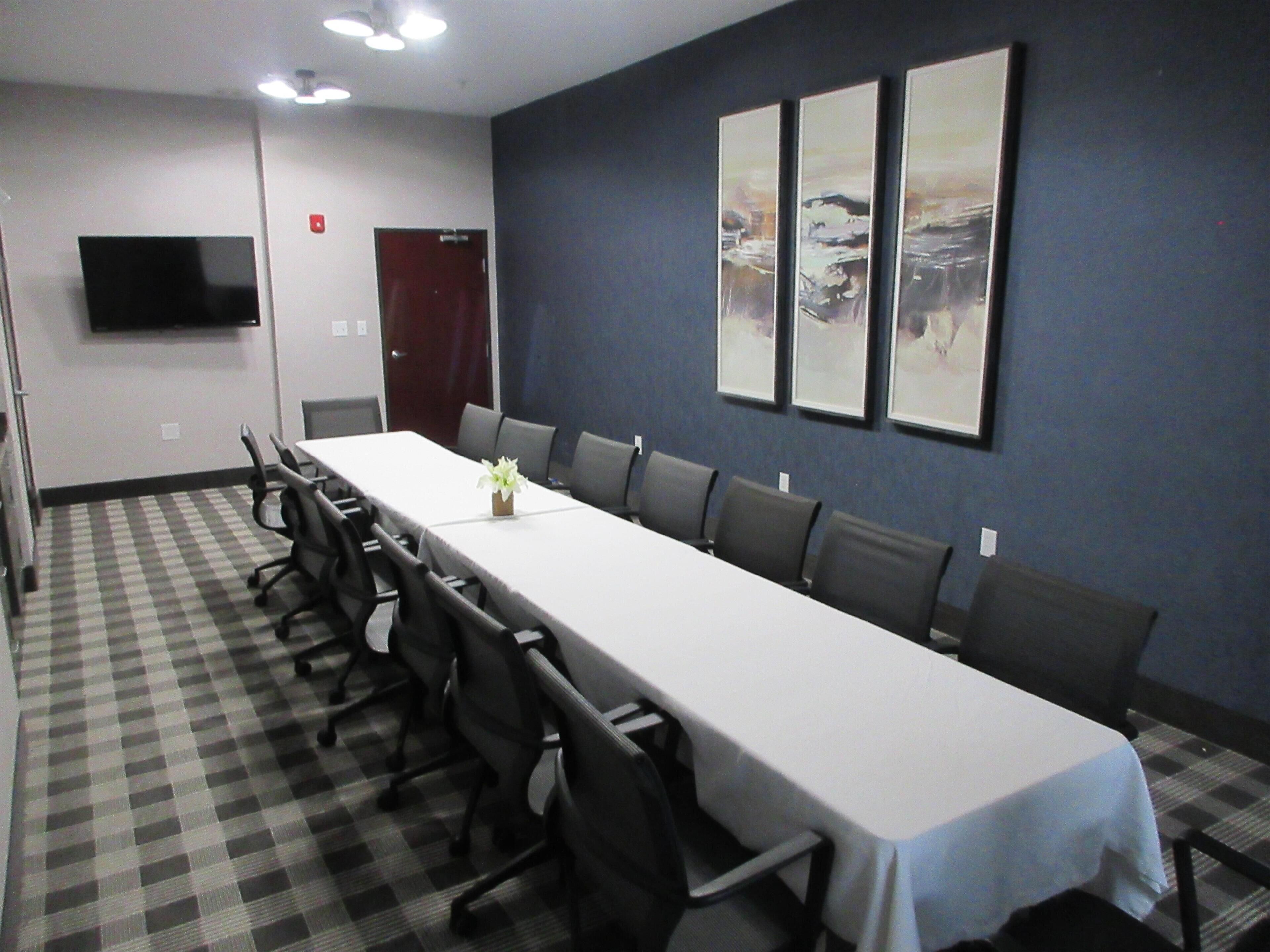 A conference room with a long table, chairs, a TV, and framed pictures on the wall.