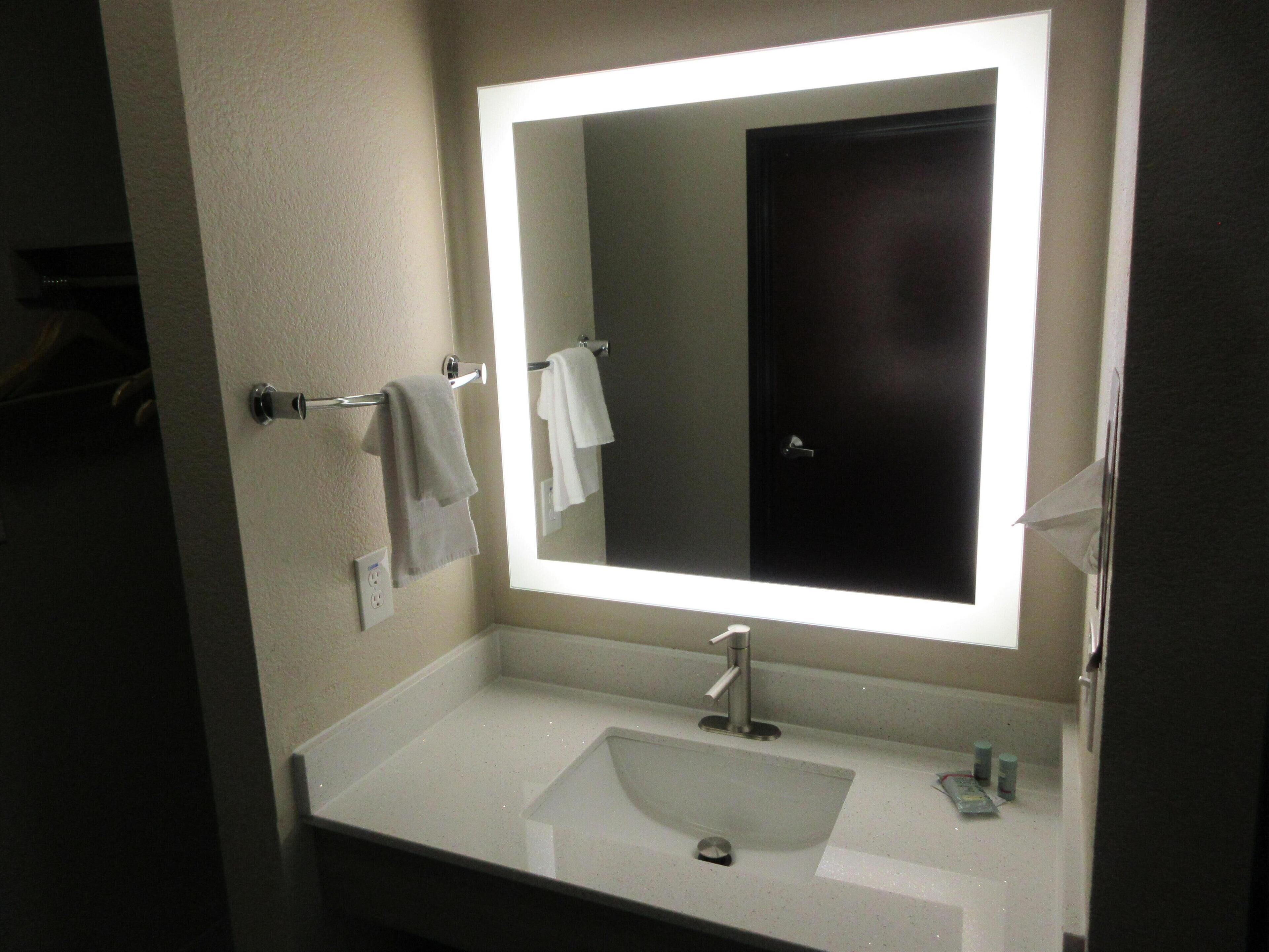 A bathroom with a white sink, a mirror with a light, and a towel rack.