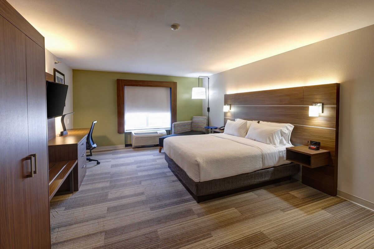 Une chambre d’hôtel comprenant un lit, une table de chevet, une lampe, une télévision et un bureau avec une chaise.