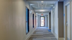 A hotel corridor with carpeted flooring, doors on both sides, and an exit sign at the end. - Holiday Inn Express & Suites Shelbyville Indianapolis by IHG (Shelbyville)
