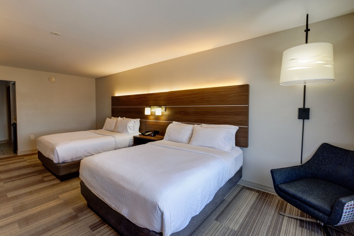 Une chambre d’hôtel avec deux lits, une table de chevet, un bureau, une chaise et une lampe.