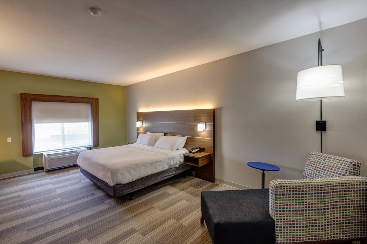 Ein Hotelzimmer mit Bett, Nachttisch, Lampe, Stuhl und einem Fenster mit Jalousien.