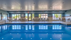 A swimming pool with chairs and tables around it, and large windows with a view of trees. - Holiday Inn Express & Suites Shelbyville Indianapolis by IHG (Shelbyville)