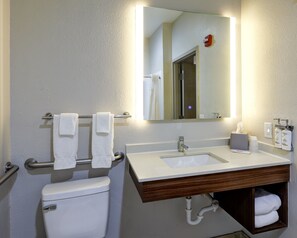 Um banheiro com pia branca, espelho, porta-toalhas com duas toalhas, vaso sanitário e dosador de sabonete.