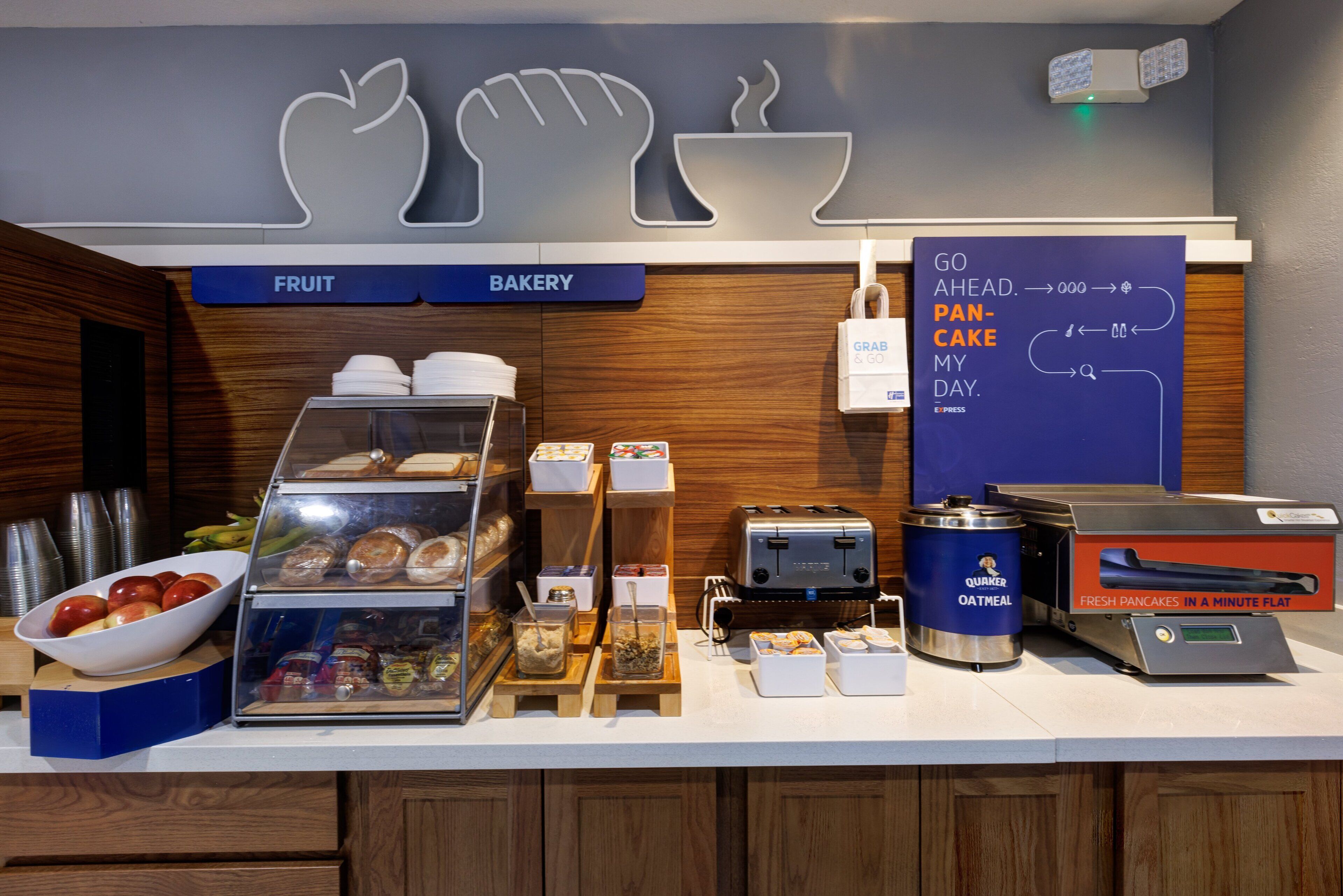 A breakfast counter with a fruit bowl, bakery section, and a sign promoting a grab-and-go breakfast option.