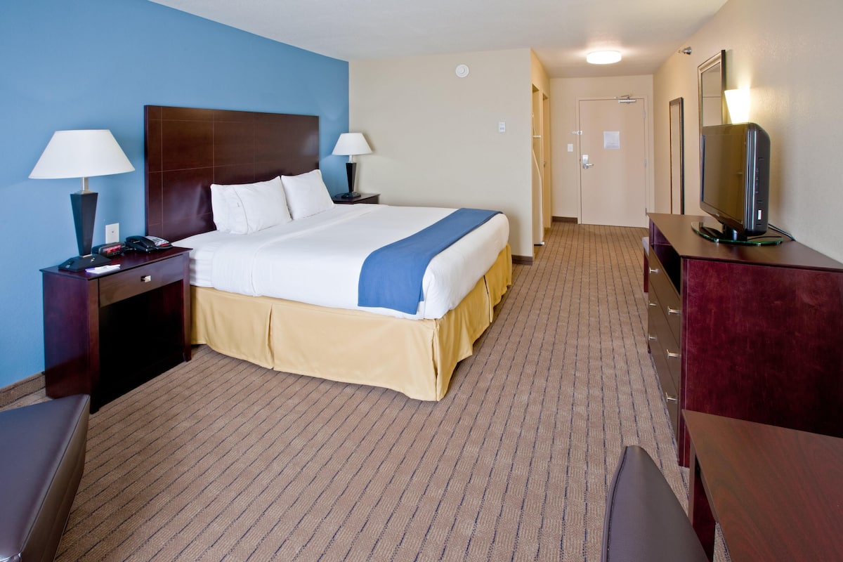 A hotel room with a large bed, bedside tables with lamps, a TV, and a mirror.