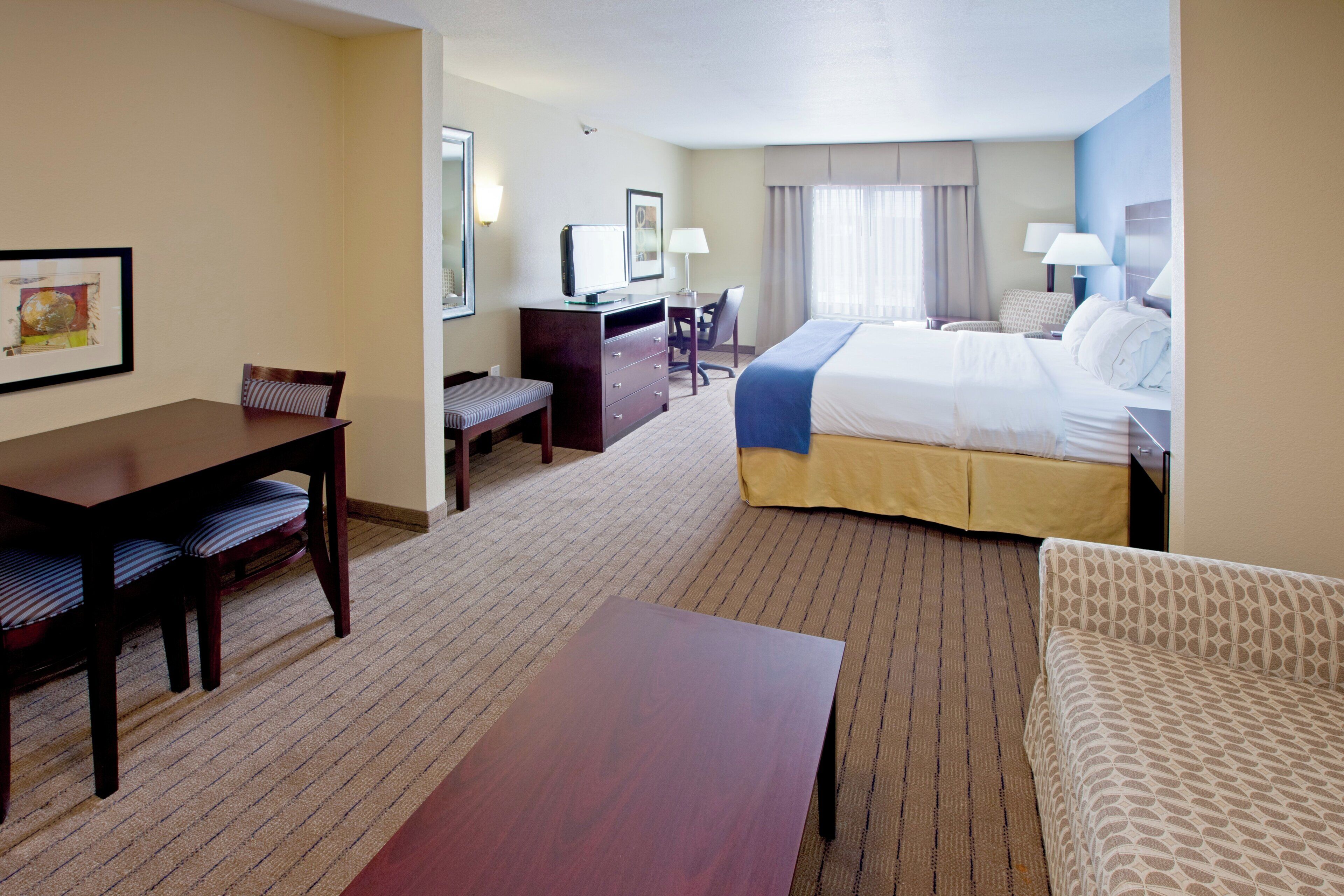 A hotel room with a bed, a desk, a chair, a small table, and a sofa.