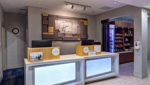 A reception desk with a modern design, a clock on the wall, and a vending machine in the background. - Holiday Inn Express & Suites Shelbyville Indianapolis by IHG (Shelbyville)
