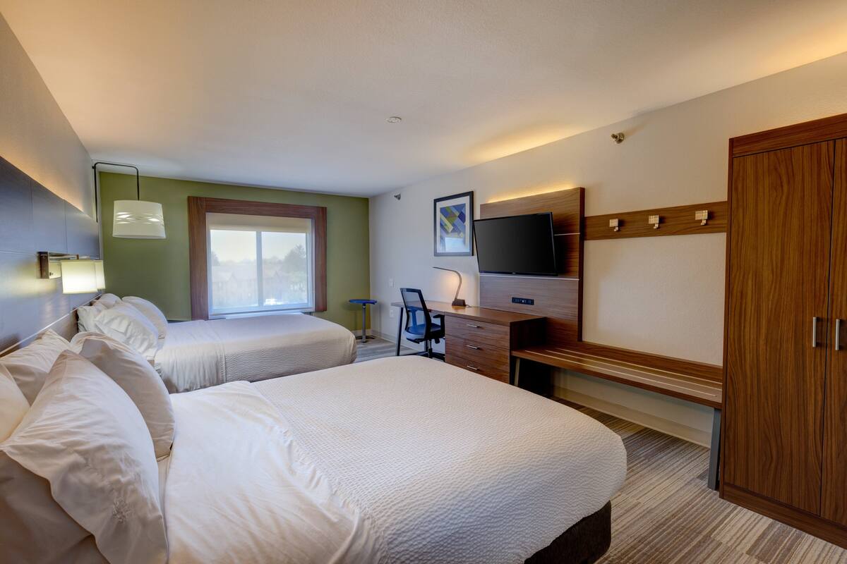 Ein Hotelzimmer mit zwei Betten, einem Schreibtisch, einem Stuhl, einem Fernseher und einem Kleiderschrank.