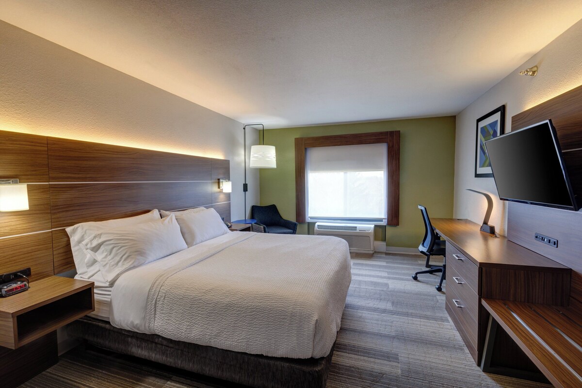Une chambre d’hôtel équipée d’un lit, d’une table de chevet, d’une lampe, d’un bureau, d’une chaise, d’une télévision et d’une fenêtre avec des stores.