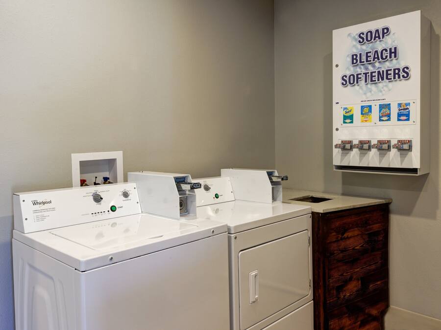 A Whirlpool washer and dryer unit with a soap, bleach, and softener dispenser mounted on the wall.